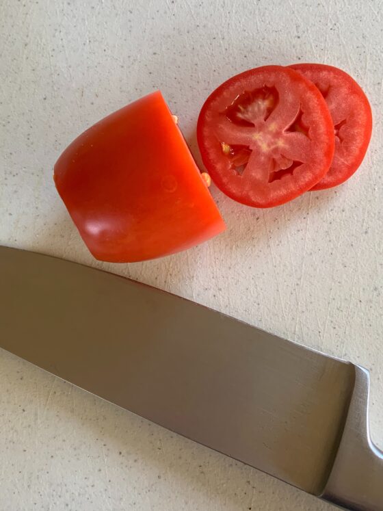 Used in photography blog tutorial. Sliced roma tomato and knife resting on cutting board.