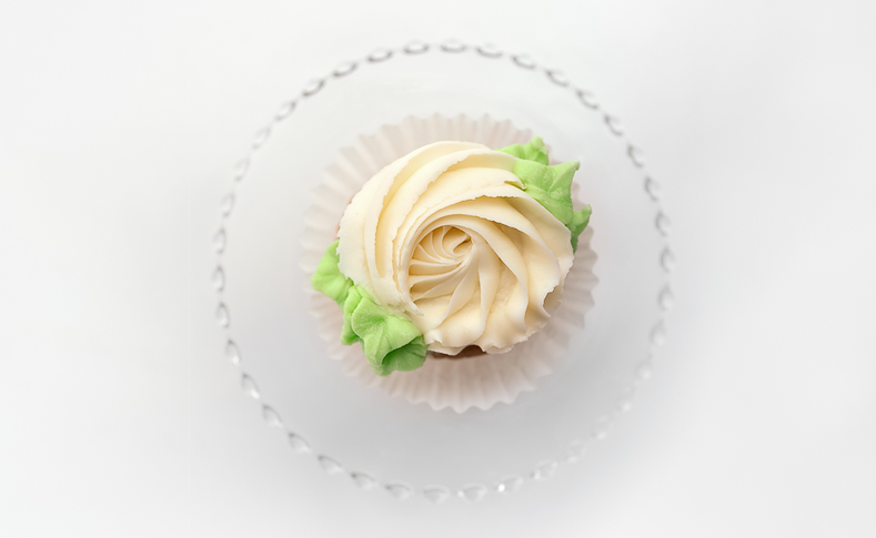 White cupcake on a small clear glass cupcake stand