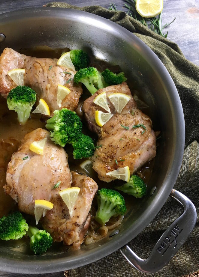 chicken thighs, lemon slices and broccoli wedges in a skillet